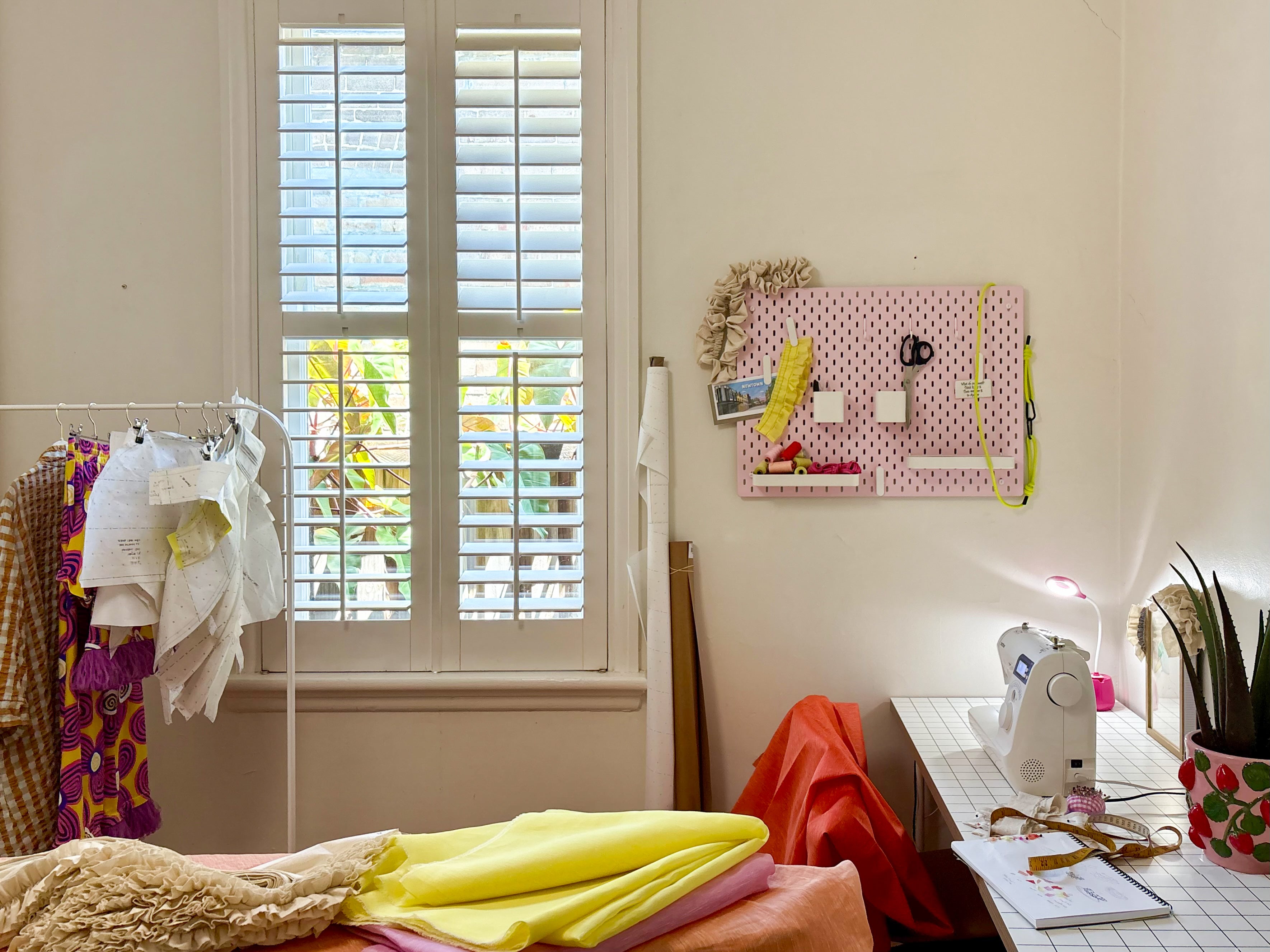 Sewing room and studio workshop with a sewing machine, deadstock fabric, and a window with white shutters. This is where La Mí Wí Magic happens.