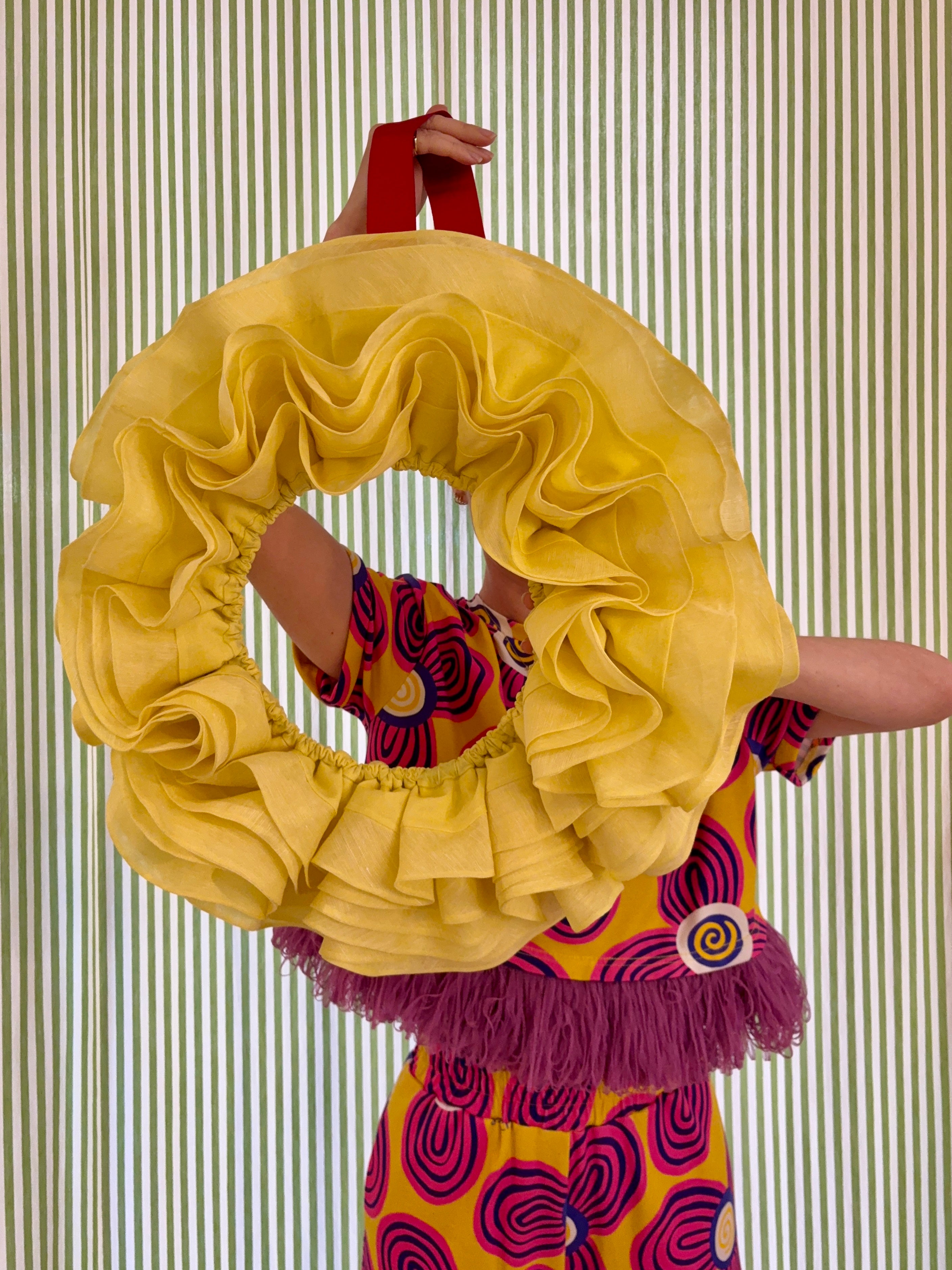 Lucy holding large frill wreath made from deadstock materials infront of a striped curtain. Deadstock to dopamine.
